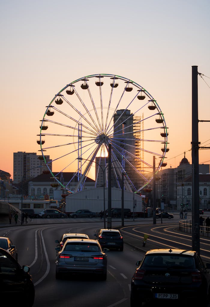 A vibrant sunset scene of a Ferris wheel in Potsdam with cars and urban buildings.
